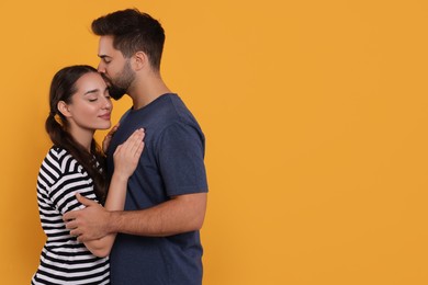 Photo of Man kissing his girlfriend on orange background. Space for text