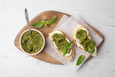 Tasty bruschettas with cream cheese, pesto sauce and fresh basil on white textured table, top view