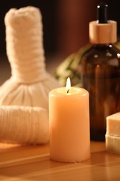 Spa composition. Cosmetic products, herbal bags and burning candle on wooden table, closeup