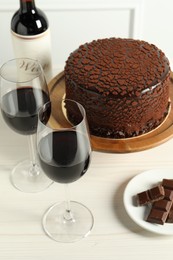 Photo of Delicious truffle cake, chocolate pieces and red wine on light wooden table