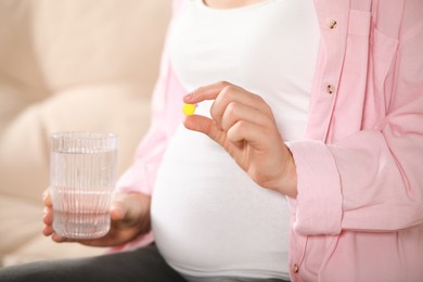 Photo of Pregnant woman holding pill and glass with water on blurred background, closeup