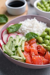 Photo of Poke bowl with salmon, edamame beans and vegetables on light grey table, closeup