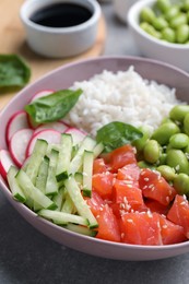 Poke bowl with salmon, edamame beans and vegetables on light grey table, closeup