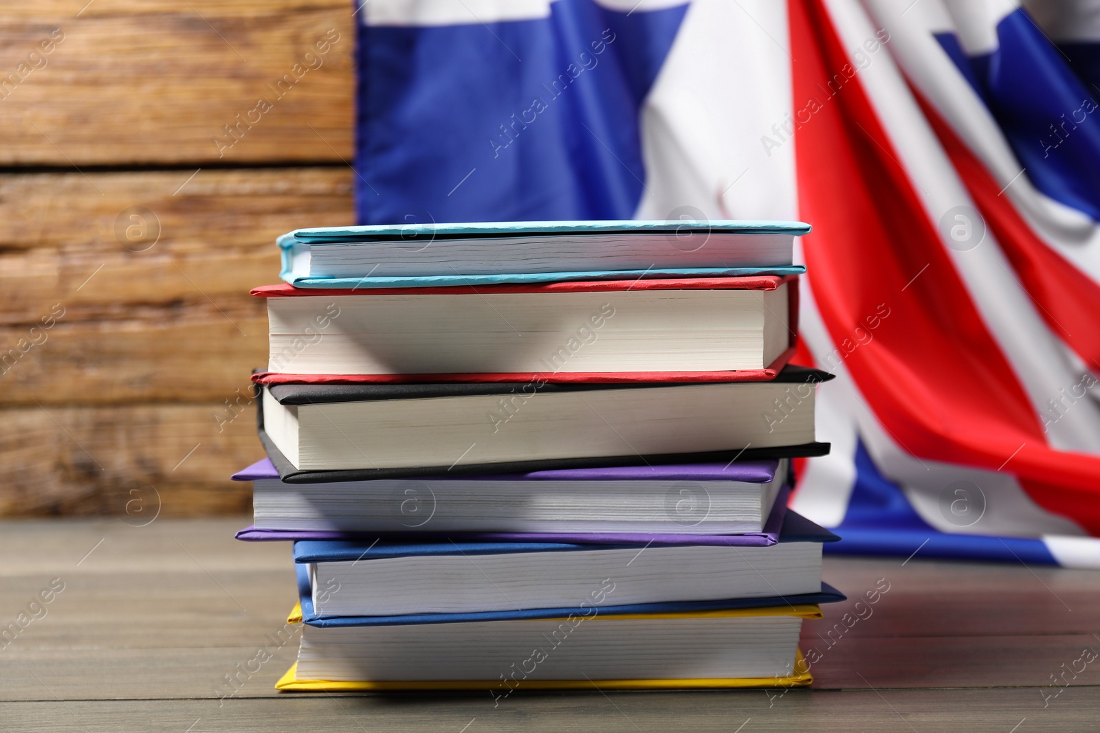 Photo of Learning foreign language. Different books on wooden table near flag of United Kingdom