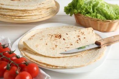 Photo of Tasty homemade tortillas, tomatoes, lettuce and knife on white wooden table