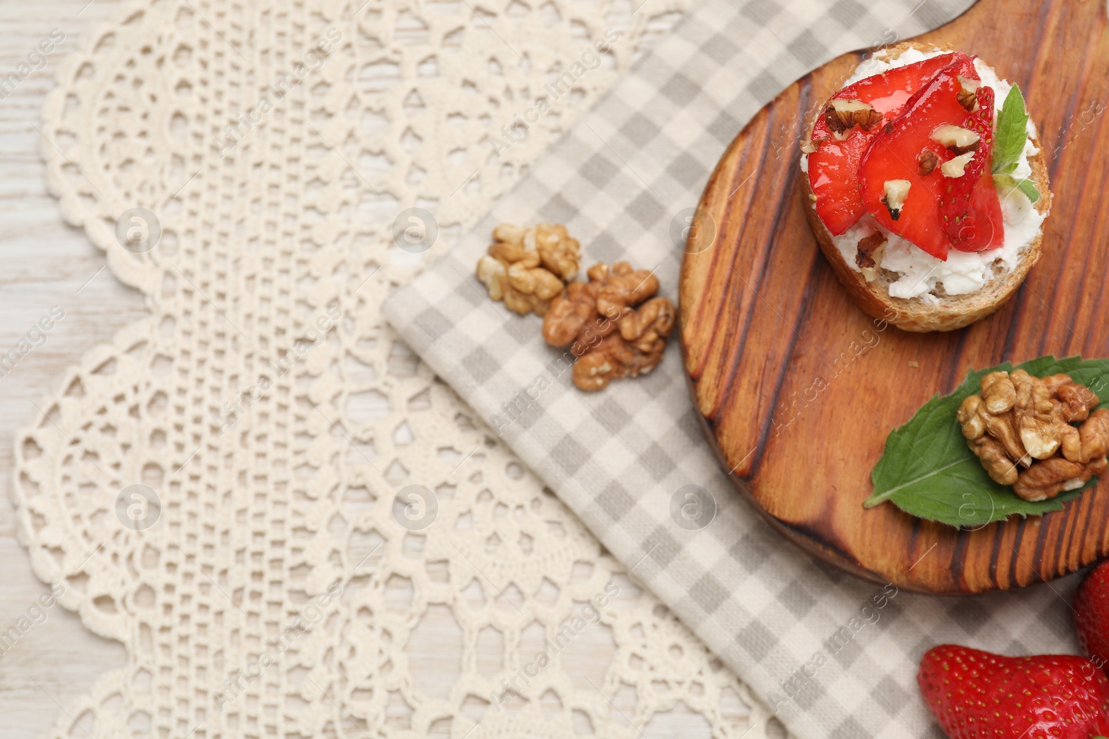 Photo of Delicious ricotta bruschetta with strawberry and walnut served on table, flat lay. Space for text