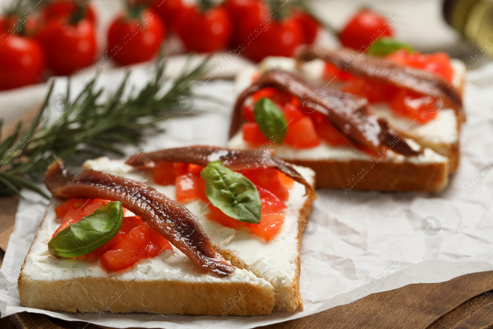 Photo of Delicious sandwiches with cream cheese, anchovies, tomatoes and basil on wooden board, closeup