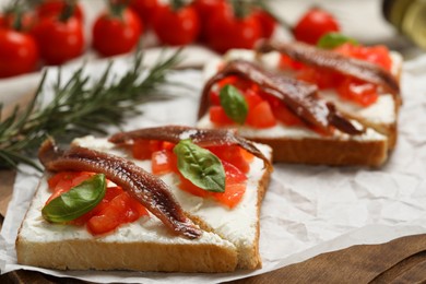 Delicious sandwiches with cream cheese, anchovies, tomatoes and basil on wooden board, closeup