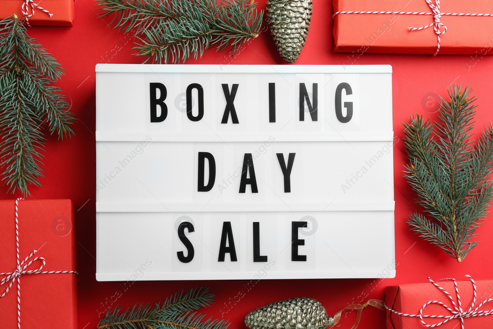 Photo of Lightbox with phrase BOXING DAY SALE and Christmas decorations on red background, flat lay