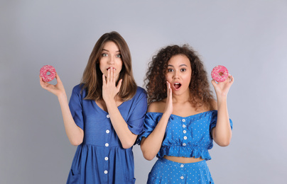 Beautiful young women with donuts on light grey background