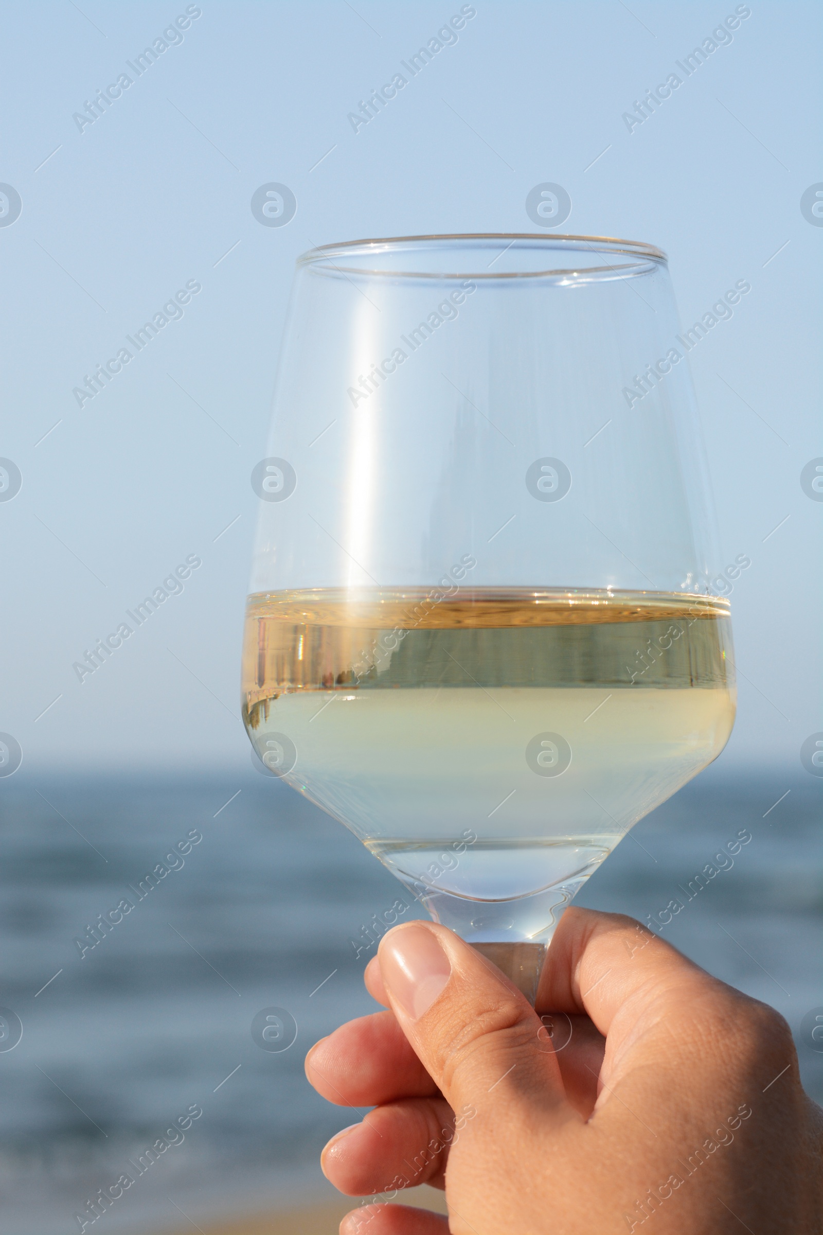 Photo of Woman holding glass of tasty wine near sea, closeup