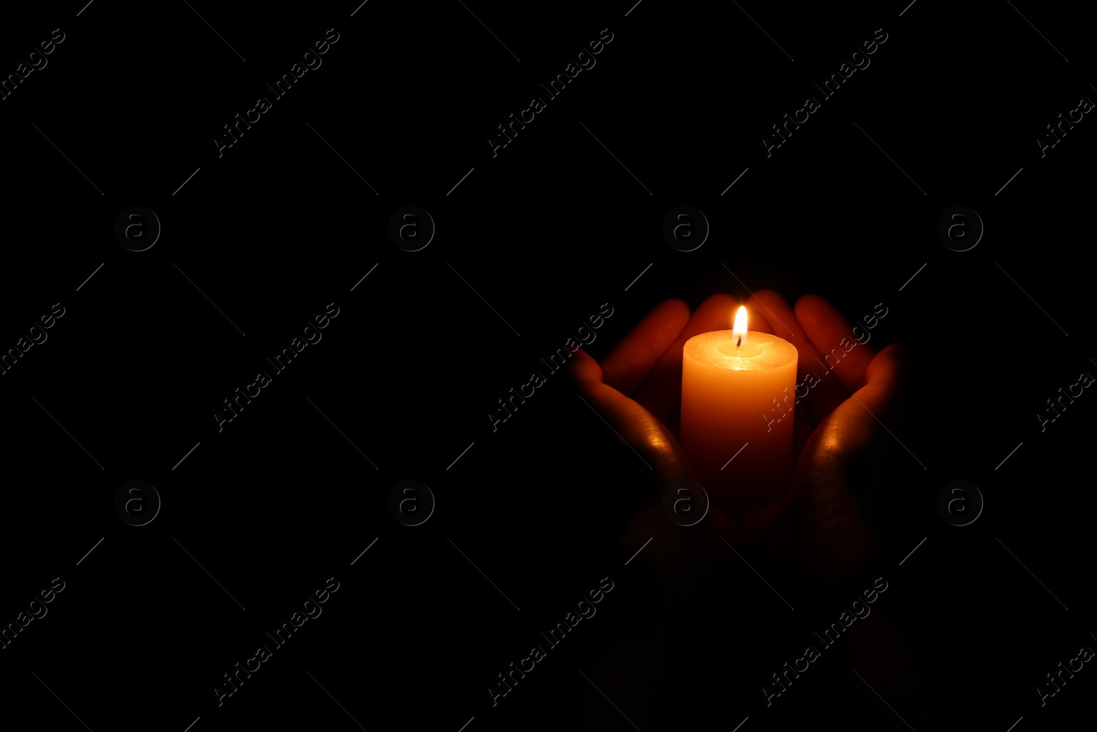 Photo of Woman holding burning candle in hands on black background, closeup. Space for text