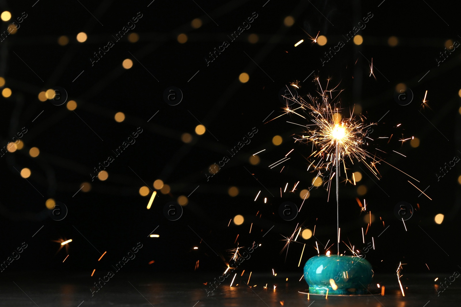 Photo of Delicious dessert with burning sparkler on table against blurred lights, space for text