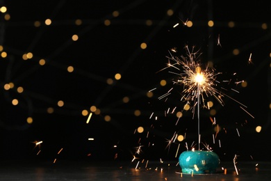 Photo of Delicious dessert with burning sparkler on table against blurred lights, space for text