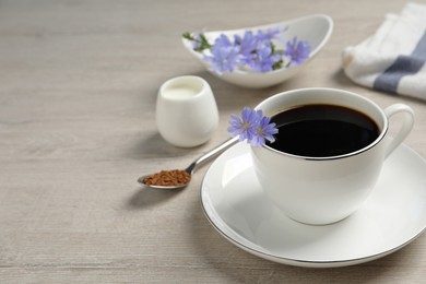 Cup of delicious chicory drink and flowers on light wooden table, space for text