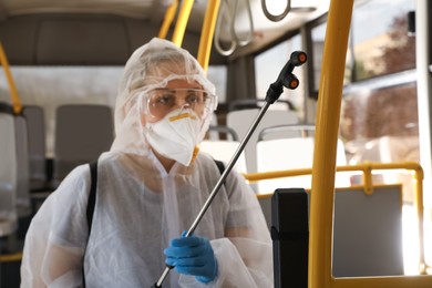 Photo of Public transport sanitation. Worker in protective suit disinfecting bus salon, focus on spray machine nozzle