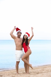 Photo of Happy young couple with Santa hats on beach near sea
