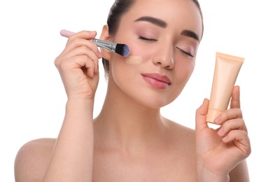 Woman with tube applying foundation on face using brush against white background