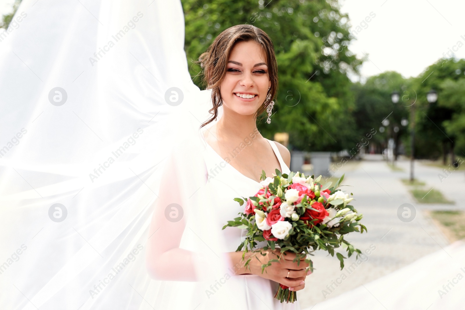 Photo of Young bride with bouquet in long veil outdoors