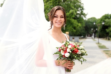Young bride with bouquet in long veil outdoors
