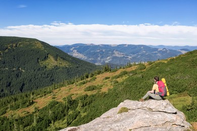 Image of Woman with backpack and sleeping mat on rocky cliff in mountains, back view