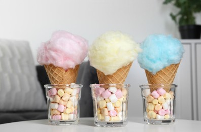 Photo of Sweet cotton candies in waffle cones and marshmallows on white table indoors, closeup