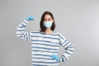 Photo of Woman with protective mask and gloves showing muscles on light grey background. Strong immunity concept