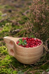 Photo of Many ripe lingonberries in wooden cup outdoors