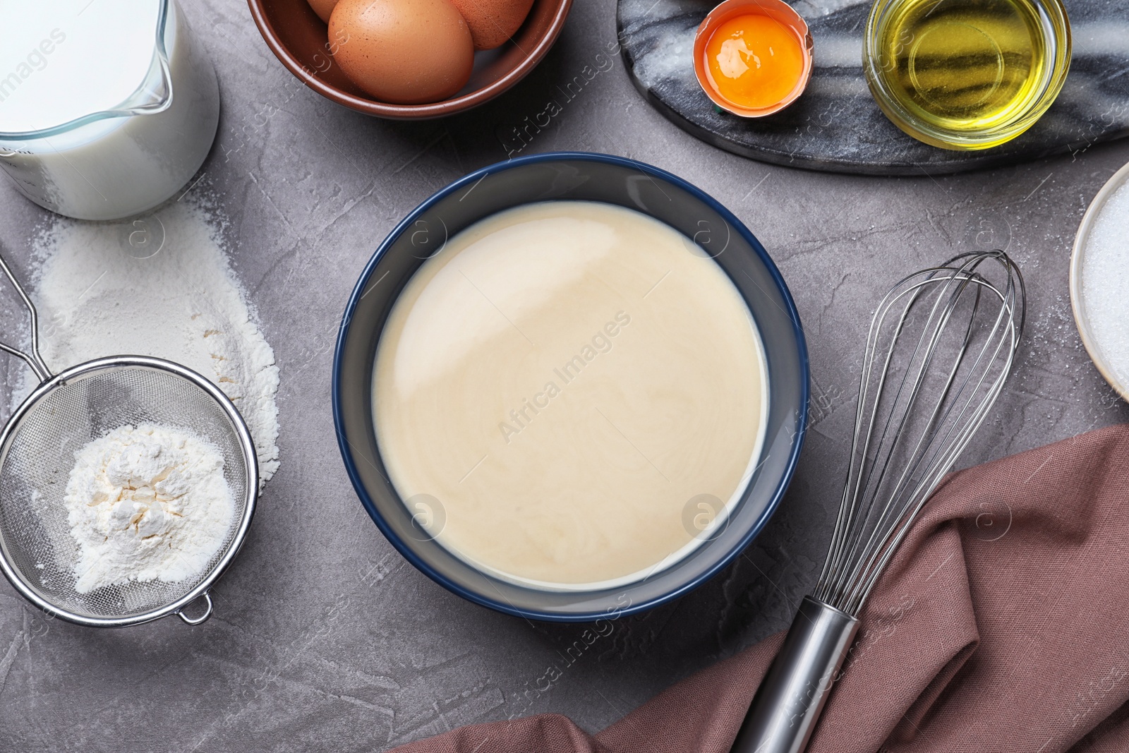 Photo of Batter for thin pancakes and products on dark grey table, flat lay