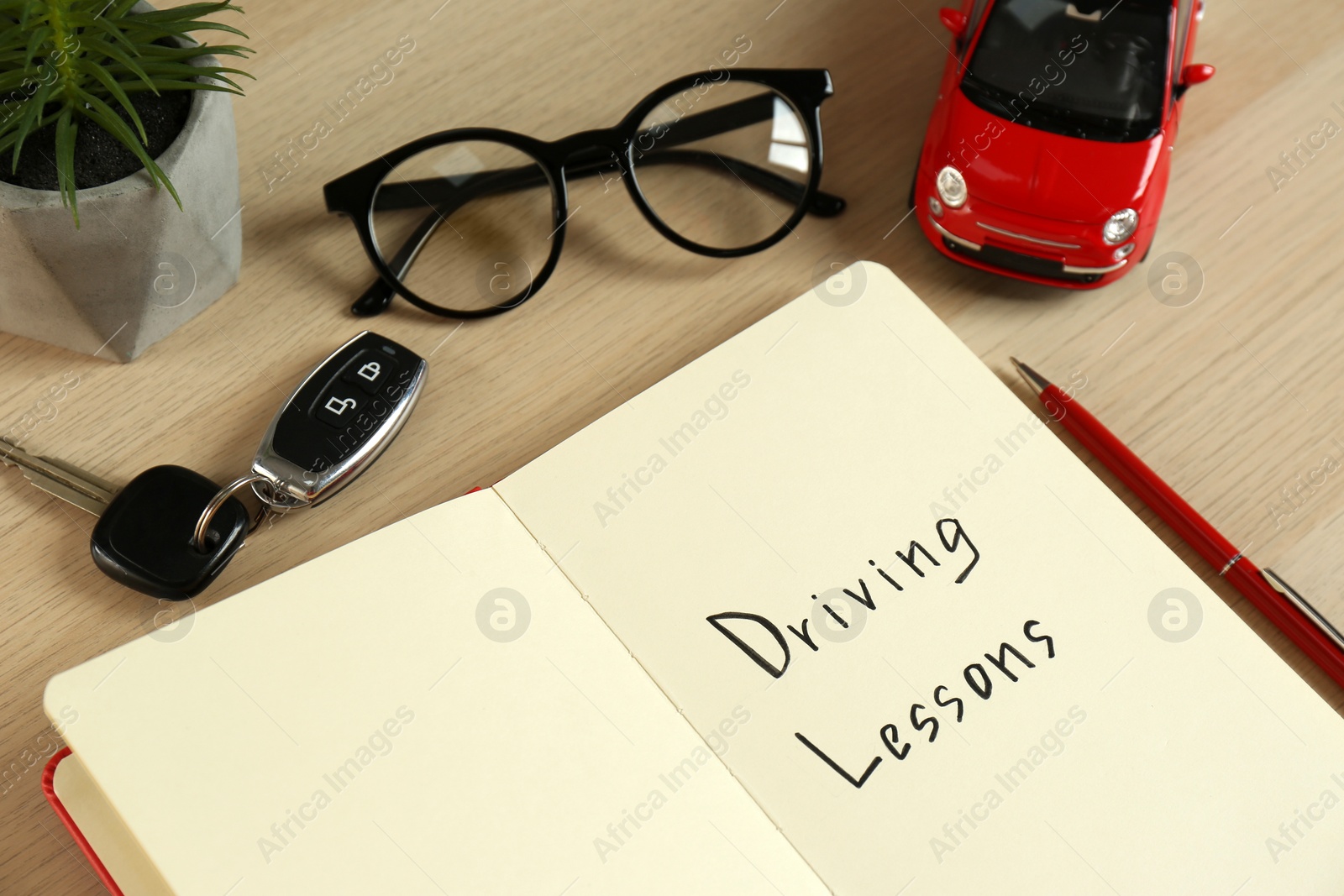 Photo of Workbook for driving lessons with pen and toy car on white wooden table. Passing license exam