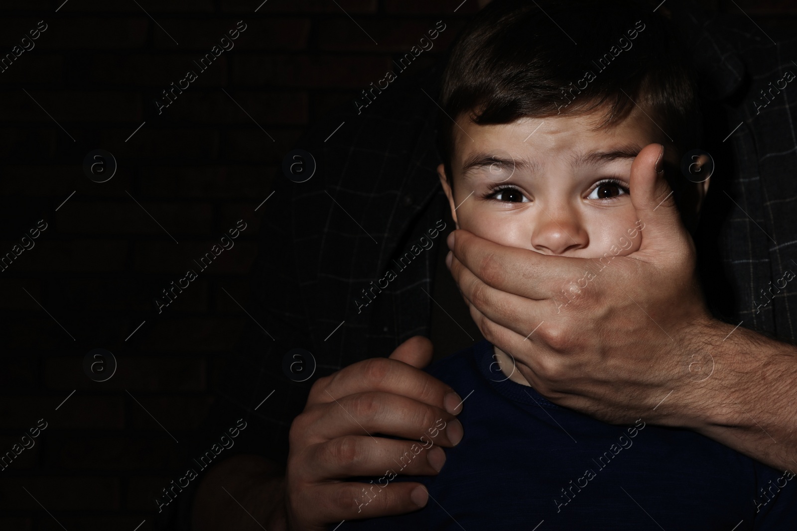 Photo of Adult man covering scared little boy's mouth on dark background, space for text. Child in danger