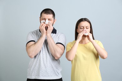 Man and woman with tissues suffering from runny nose on light grey background