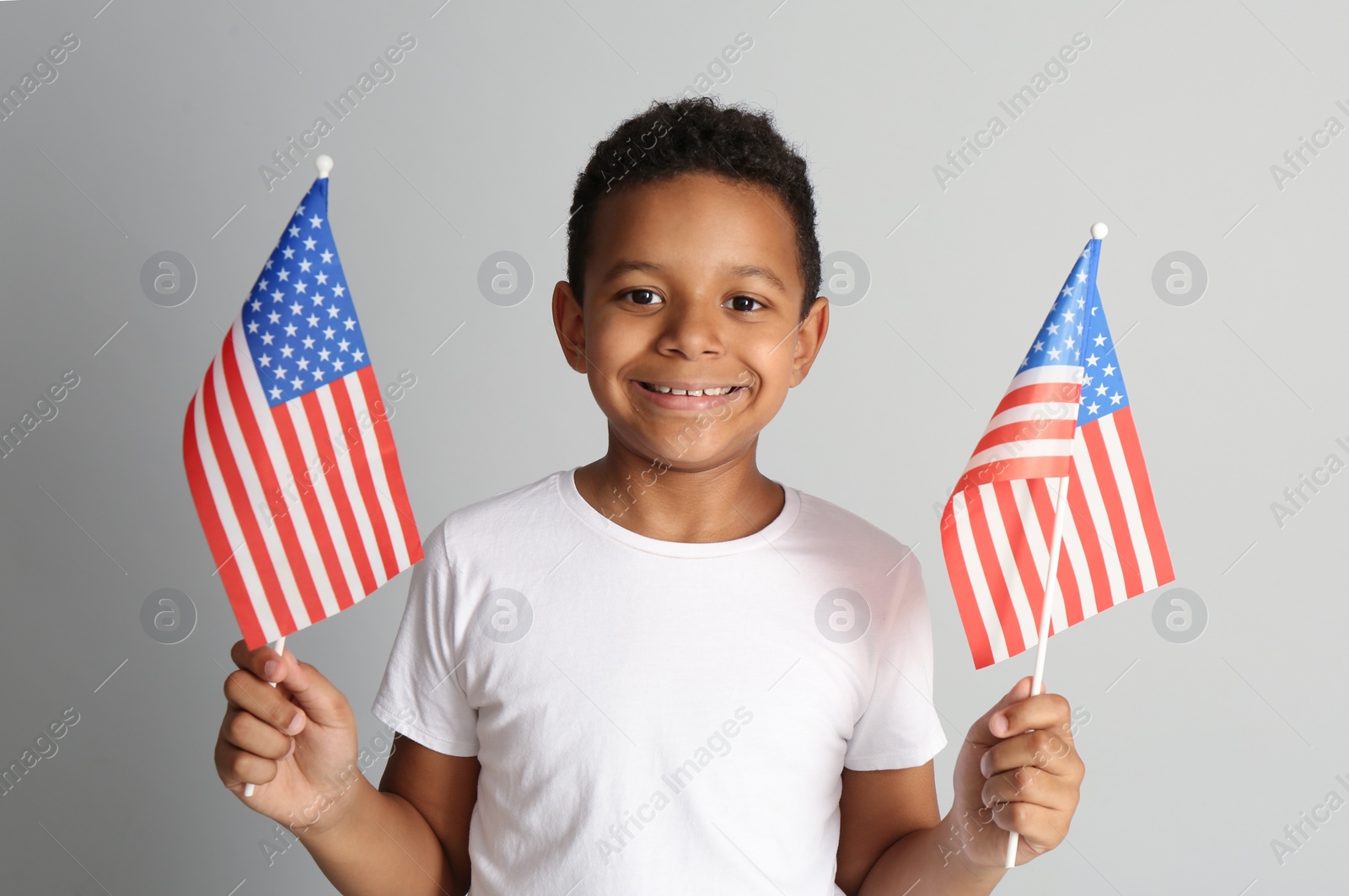 Photo of Happy African-American boy holding national flags on light grey background