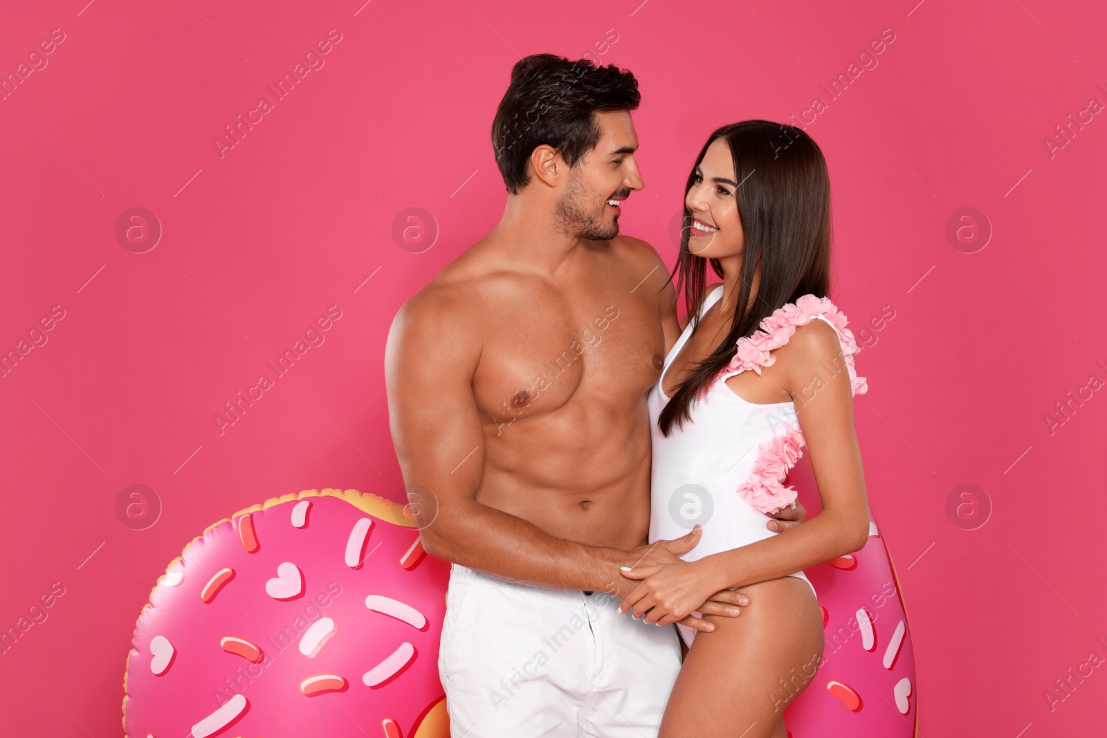 Photo of Young attractive couple in beachwear with inflatable ring on pink background