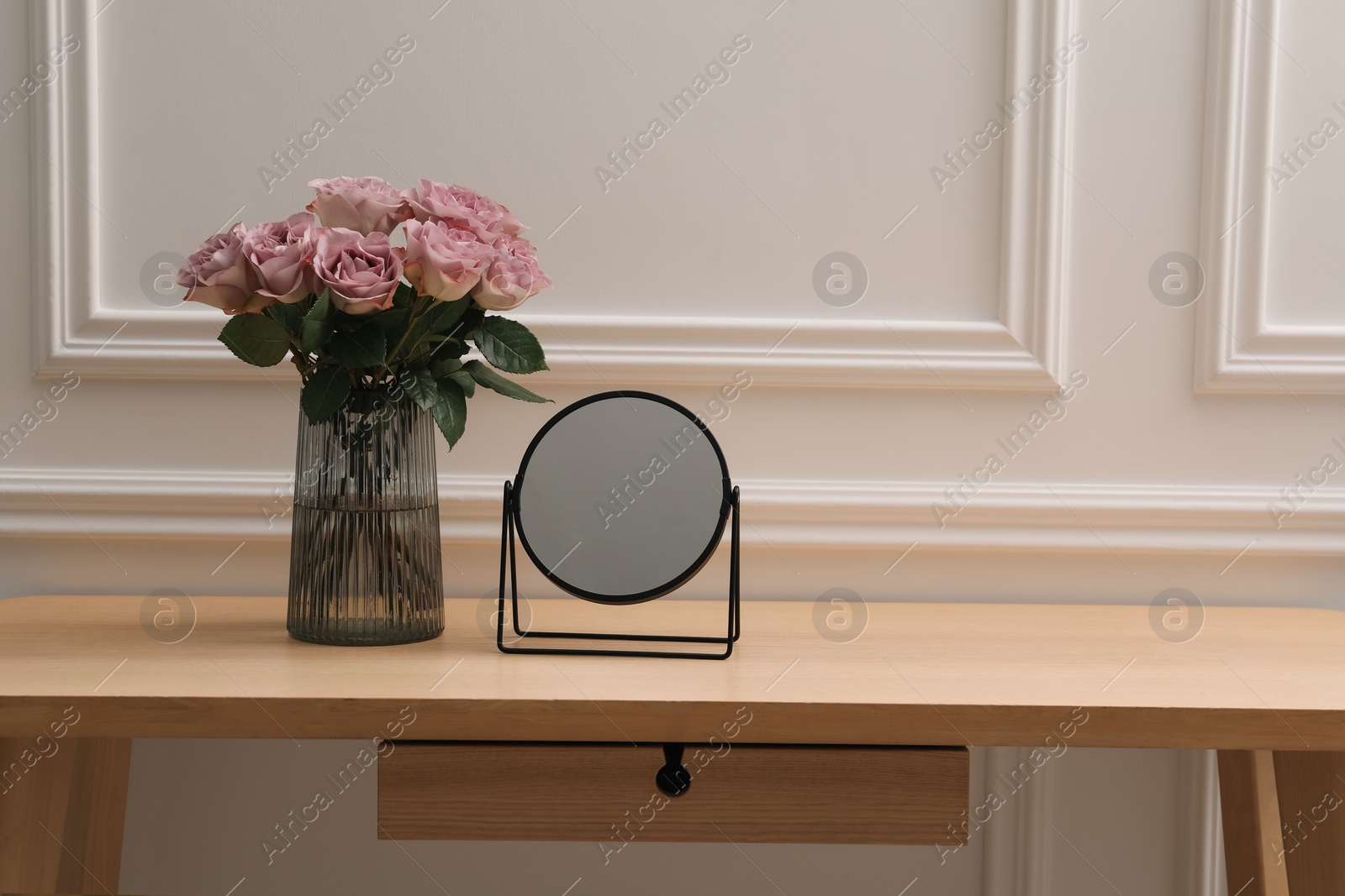 Photo of Mirror and vase with pink roses on wooden dressing table in makeup room, space for text