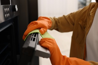 Photo of Woman with microfiber cloth cleaning electric oven in kitchen, closeup