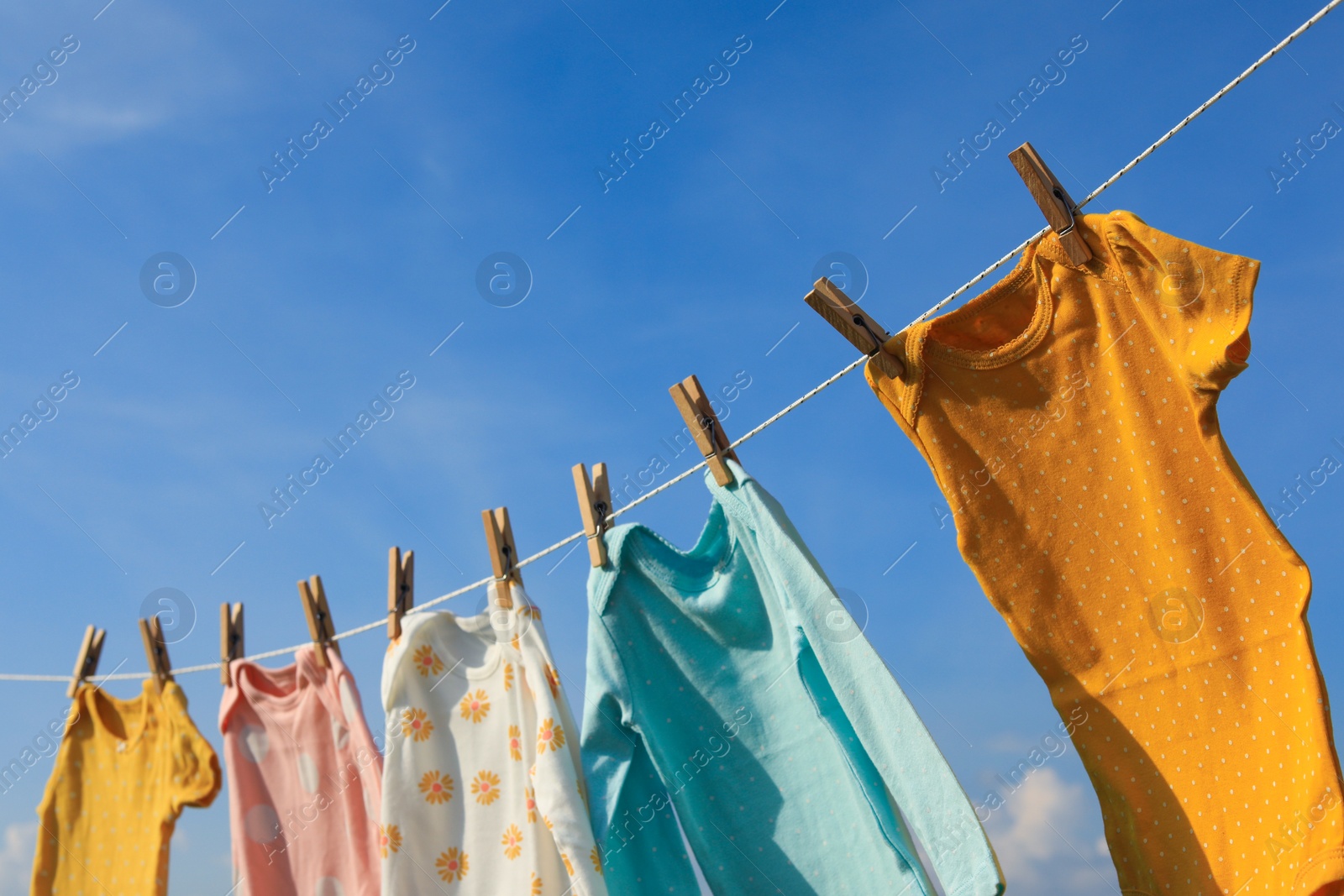 Photo of Clean baby onesies hanging on washing line against sky. Drying clothes