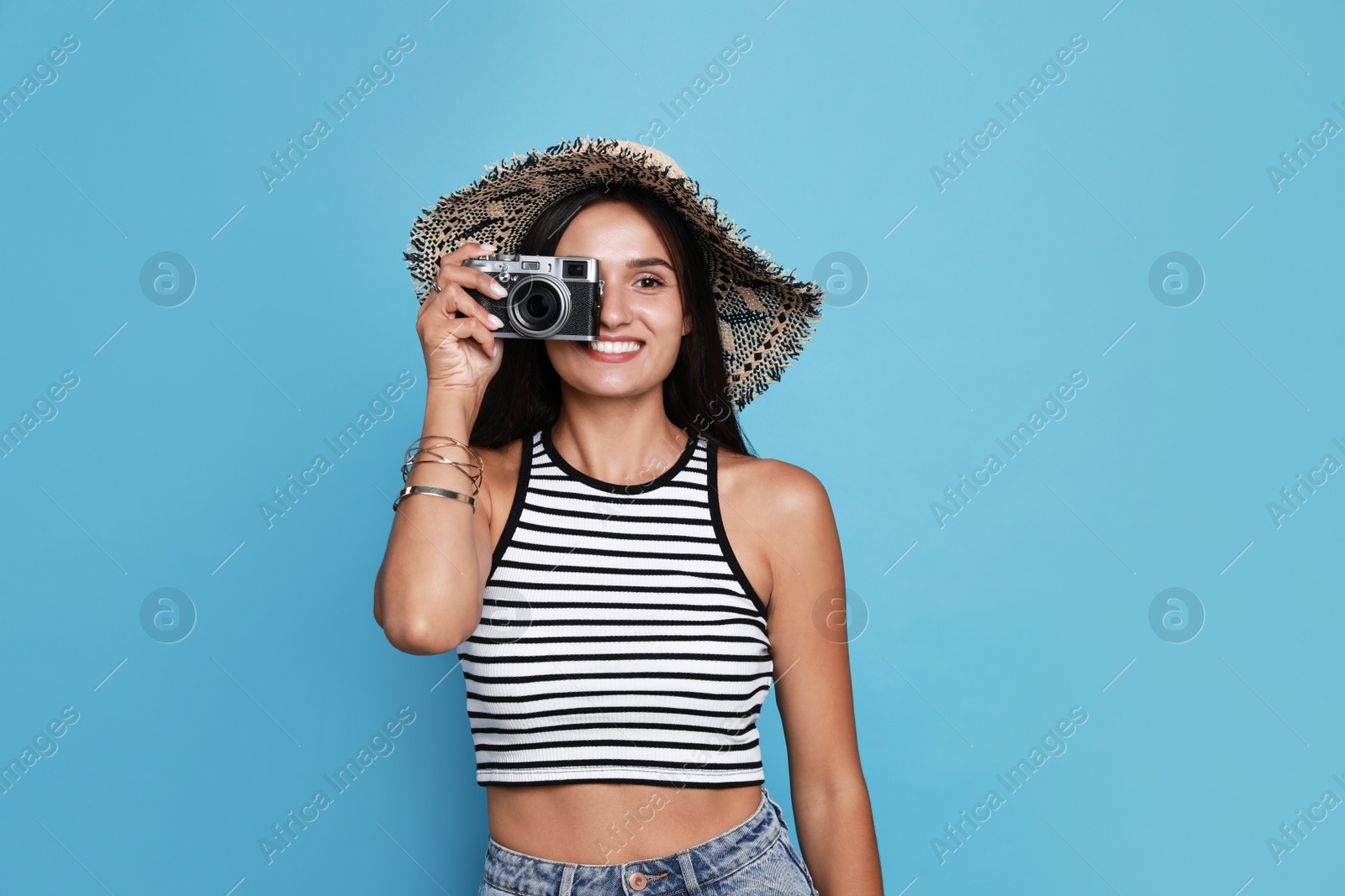 Photo of Beautiful young woman with straw hat and camera on light blue background