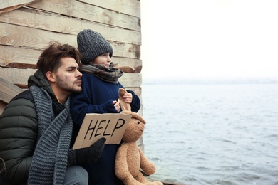 Photo of Poor father and child with HELP sign at riverside. Space for text