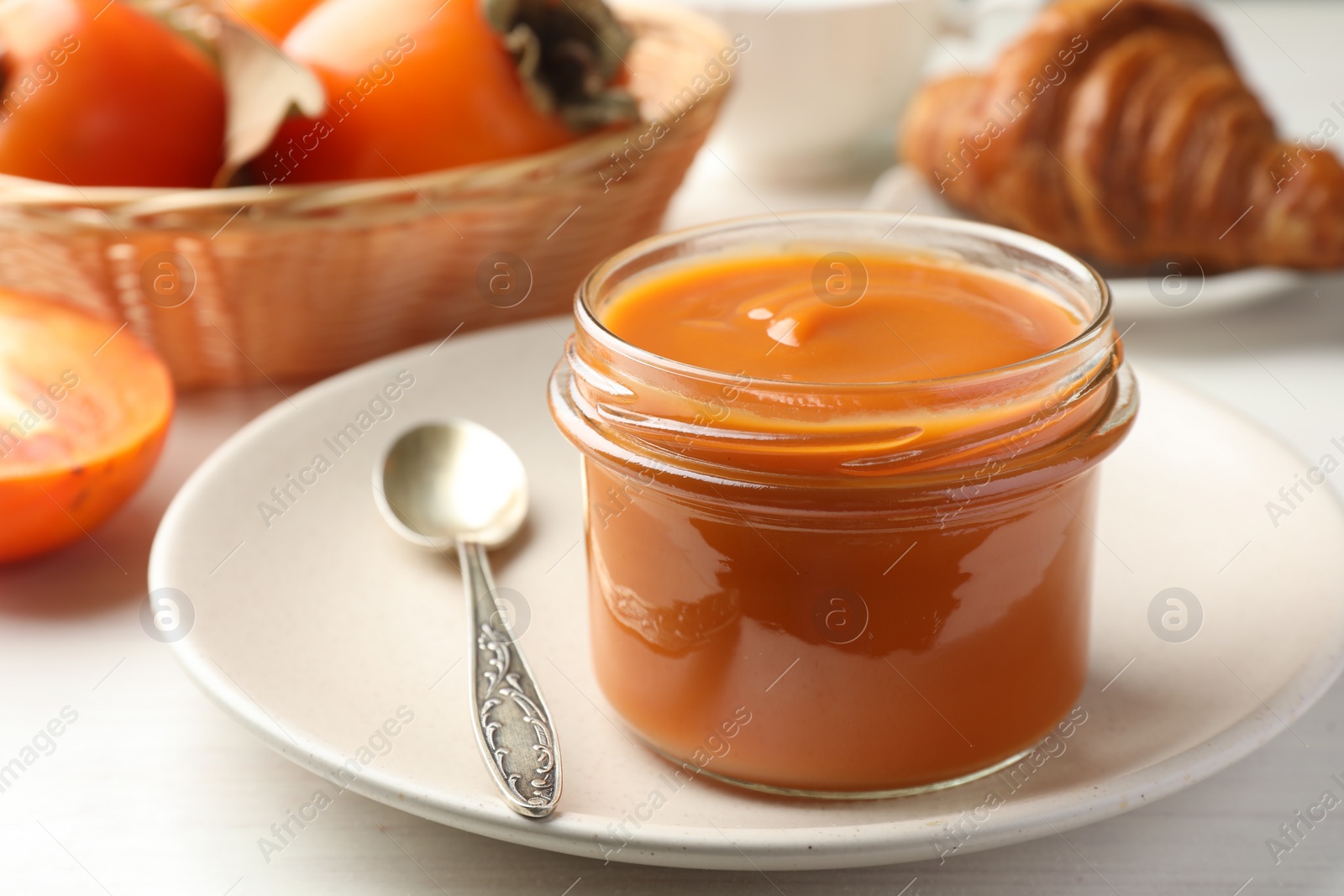 Photo of Delicious persimmon jam in glass jar served on white wooden table, closeup