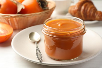 Delicious persimmon jam in glass jar served on white wooden table, closeup