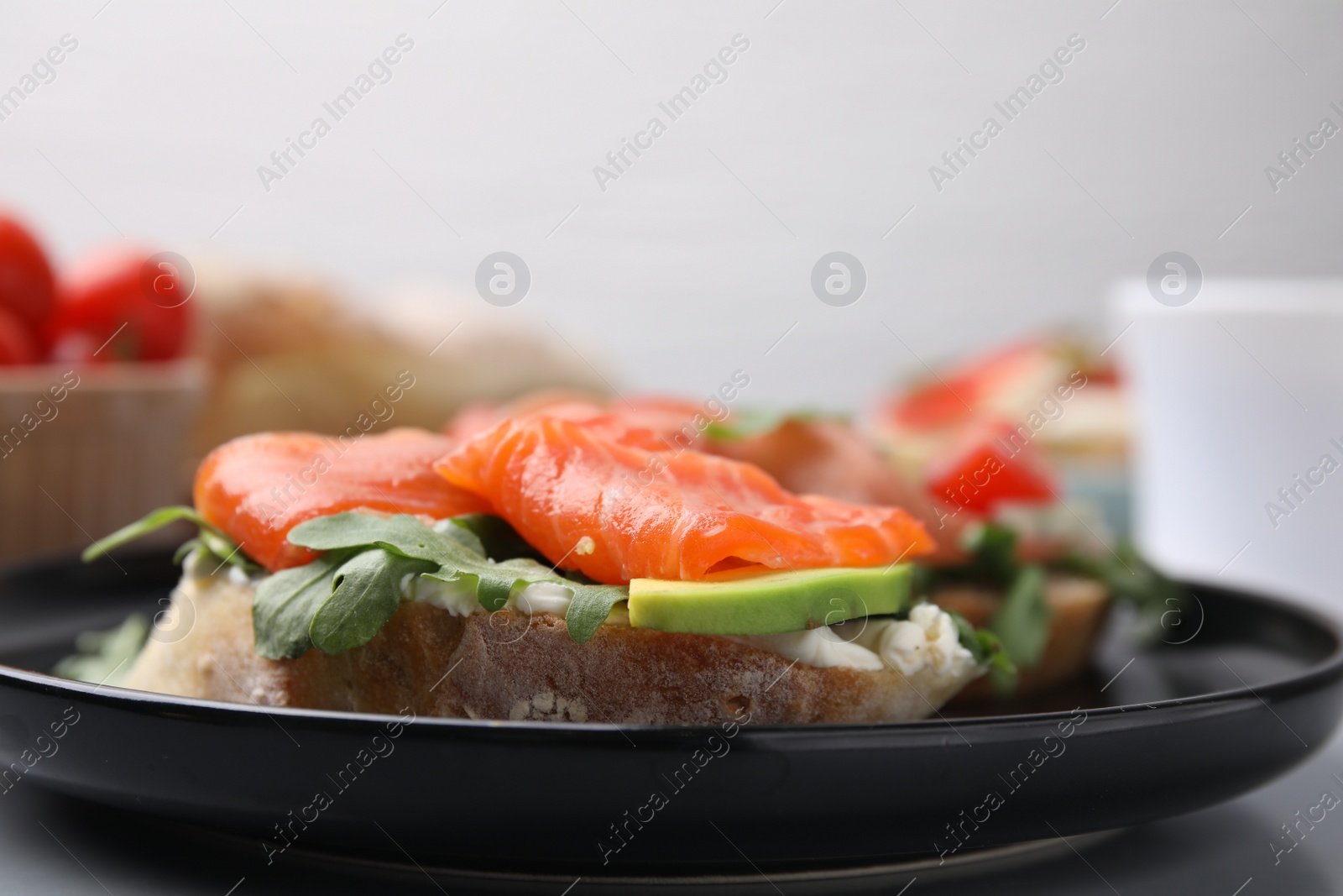 Photo of Tasty bruschetta with salmon, arugula and avocado on black plate, closeup