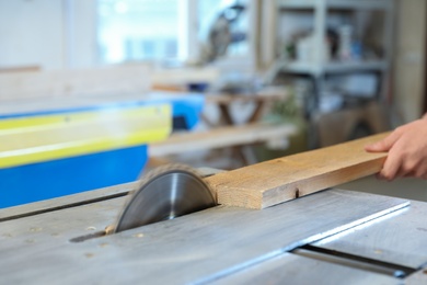 Photo of Working man using circular saw at carpentry shop, closeup