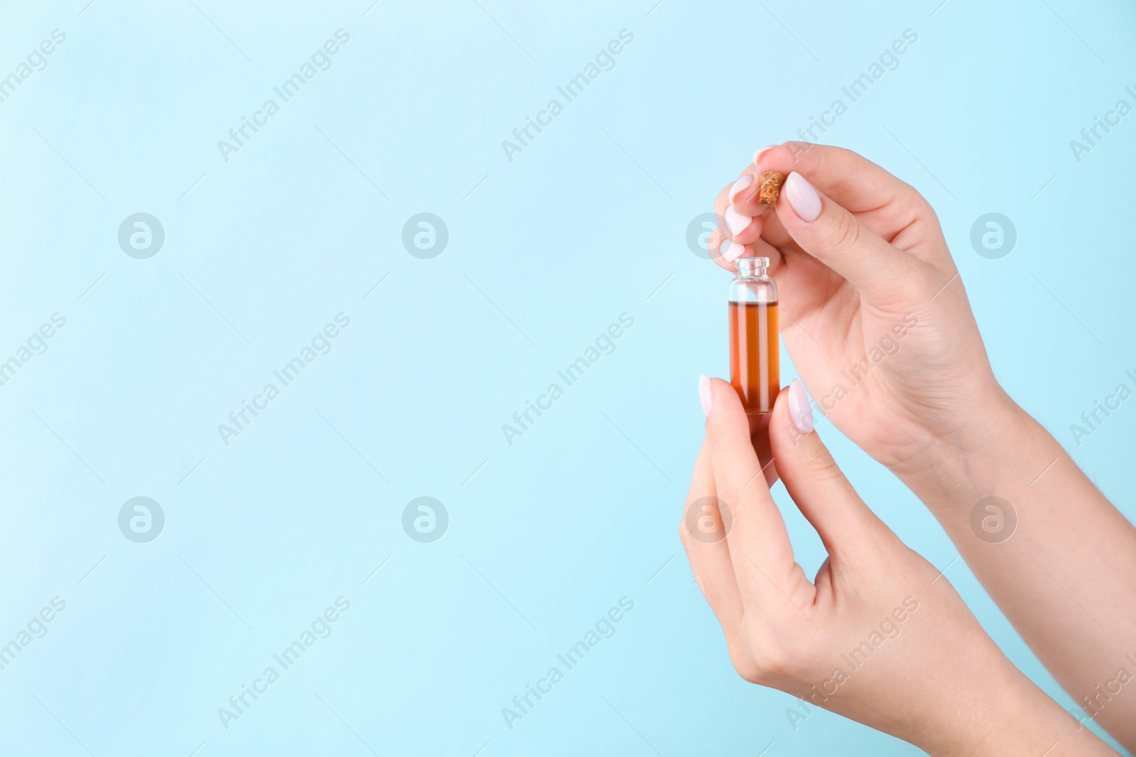 Photo of Woman holding bottle of essential oil on light blue background, closeup. Space for text