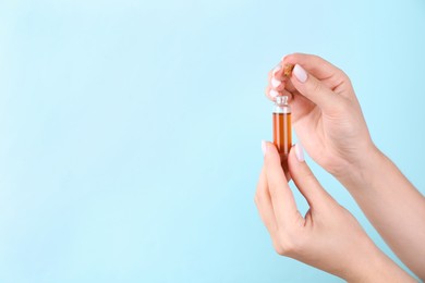Photo of Woman holding bottle of essential oil on light blue background, closeup. Space for text