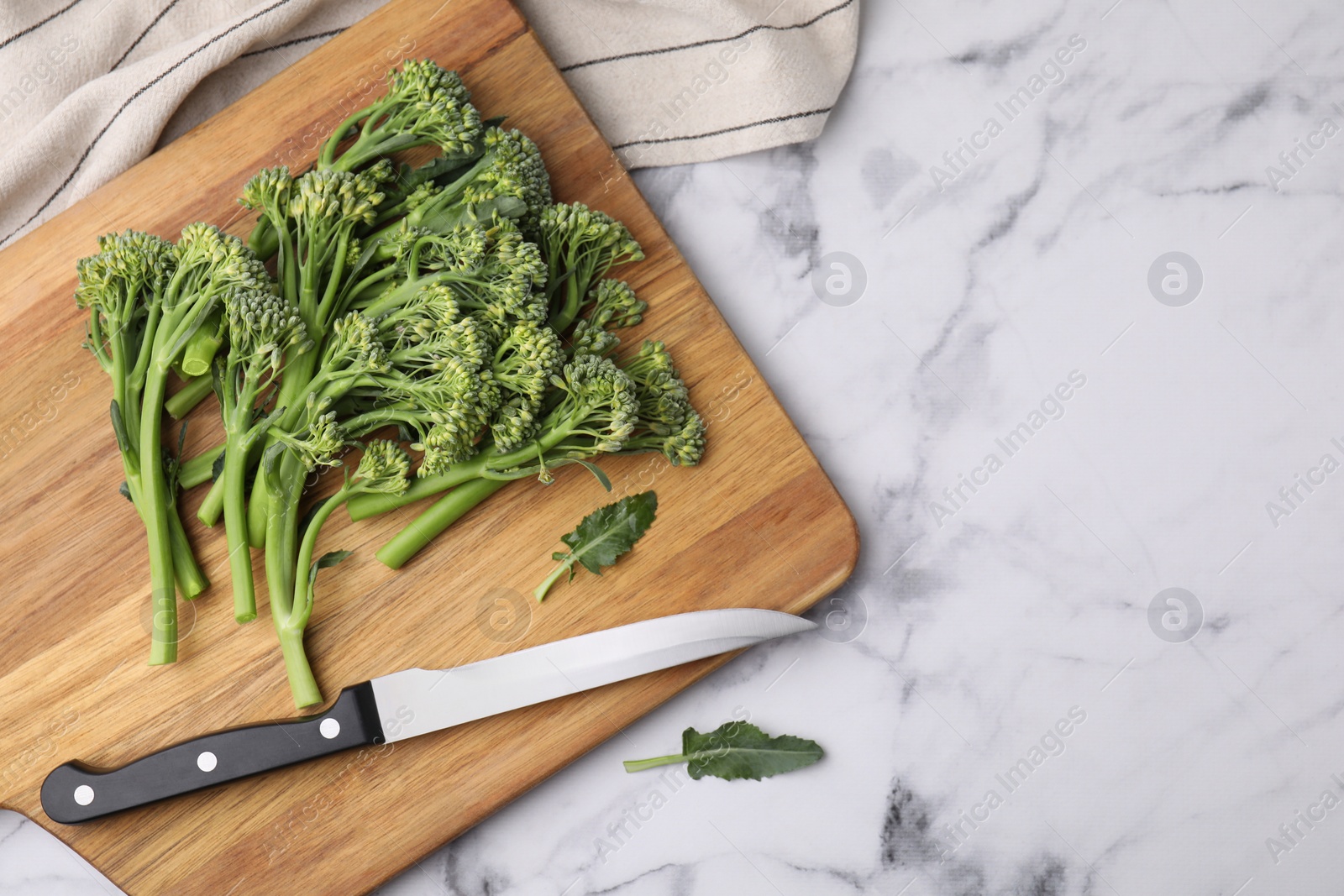 Photo of Fresh raw broccolini and knife on white marble table, flat lay with space for text. Healthy food