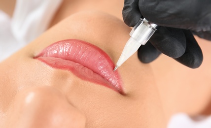 Photo of Young woman getting permanent makeup on lips in beautician salon, closeup