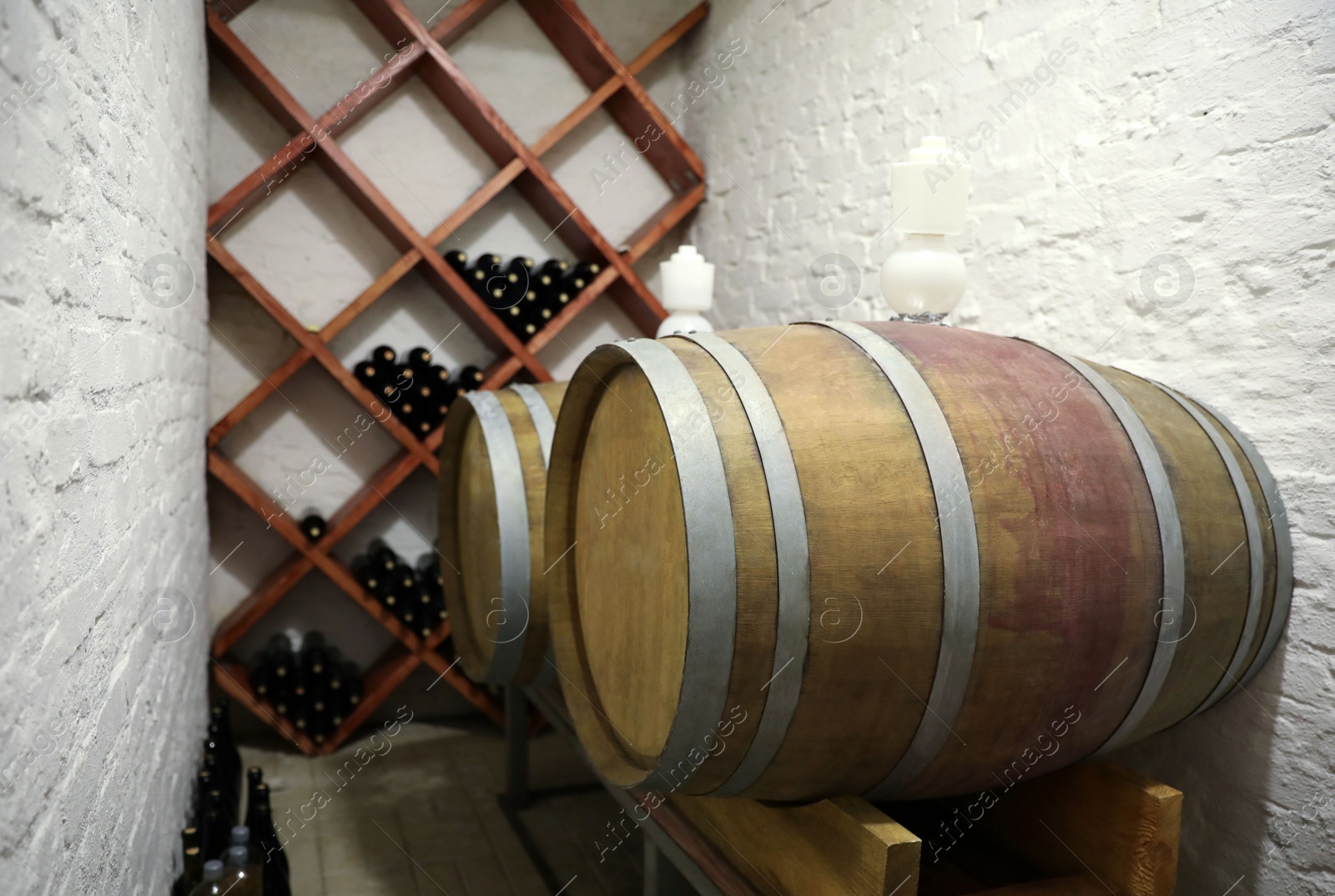 Photo of Wooden barrels on stand near white brick wall in wine cellar