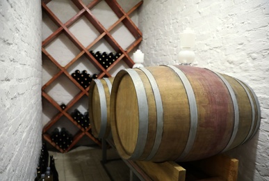 Photo of Wooden barrels on stand near white brick wall in wine cellar