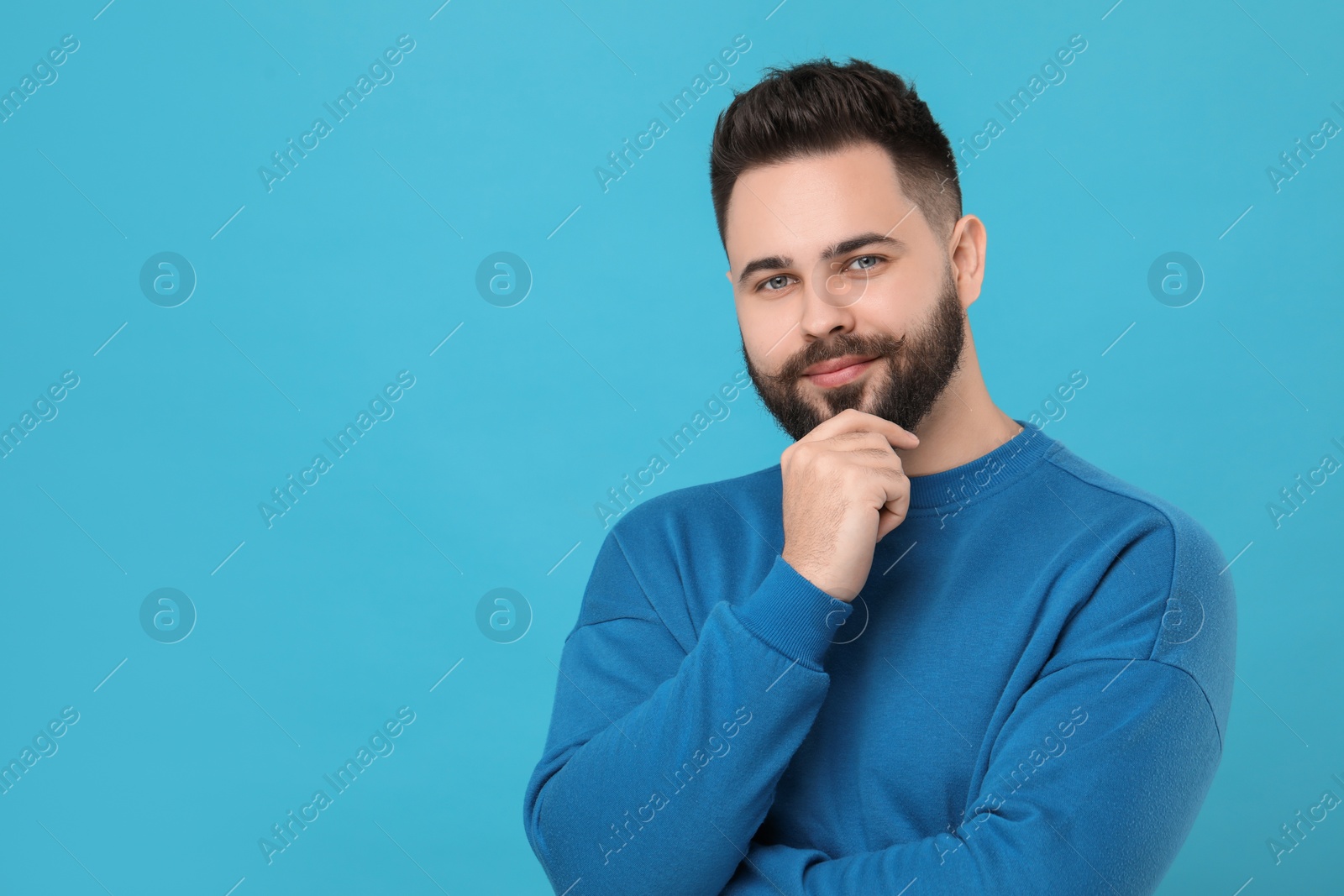 Photo of Young man with mustache touching face on light blue background. Space for text